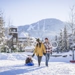 A family walks through a winter landscape pulling a child on a sled